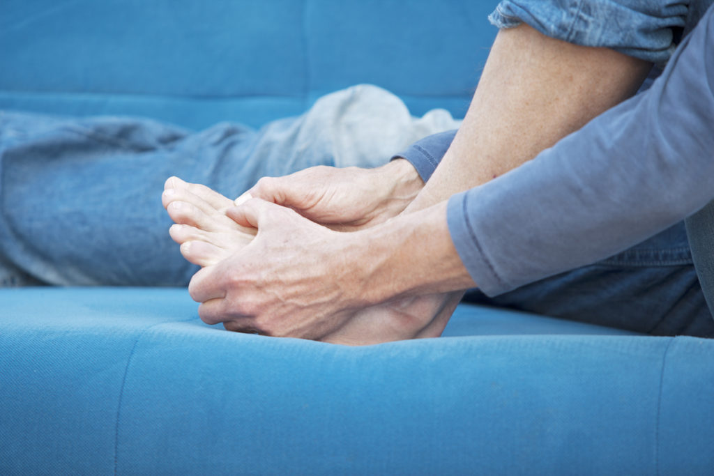Woman sitting down on the couch holding her foot in pain.
