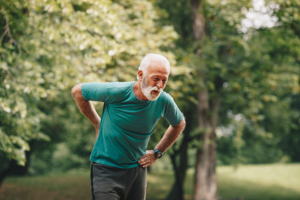 Sporty senior man having back pain while jogging.