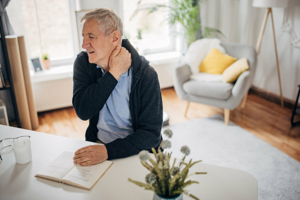 A man is experiencing chronic neck pain while sitting at his work desk.