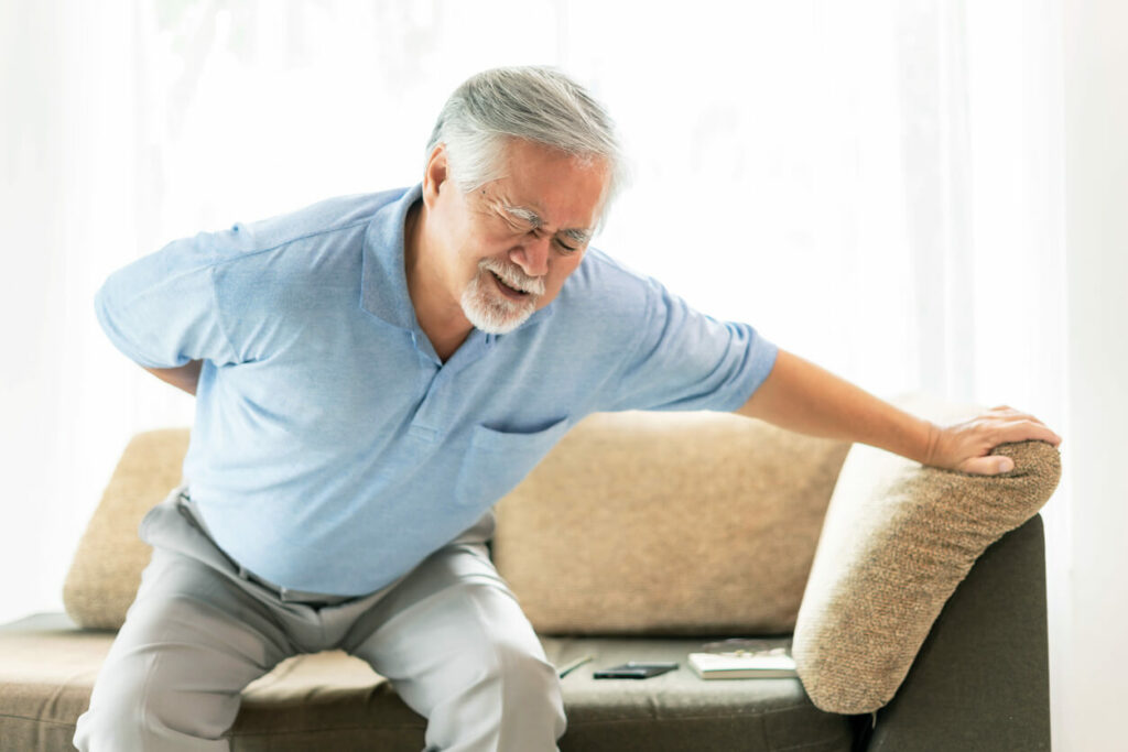 An elderly man on the couch, about to stand up, is suffering from back pain.