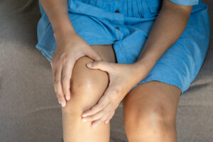 A woman's knee pain causes her to place her hands on her knees, which is a sign of meniscus tear symptoms.
