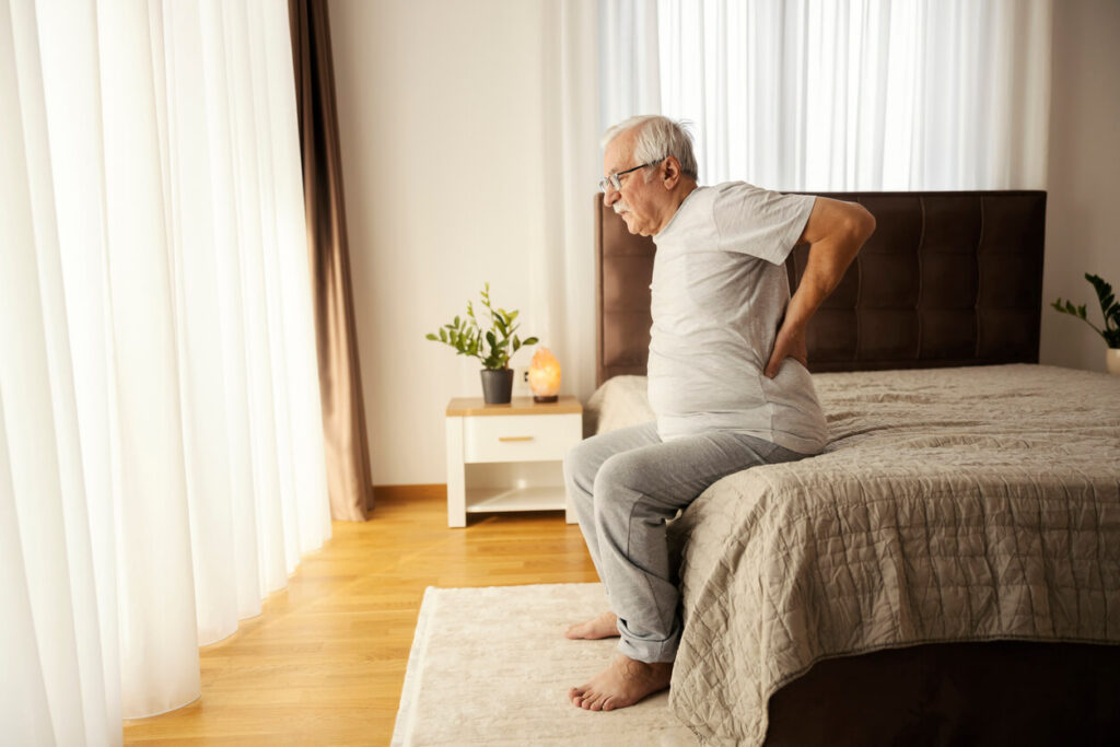 Senior man with backache trying to get up from the bed in the morning.